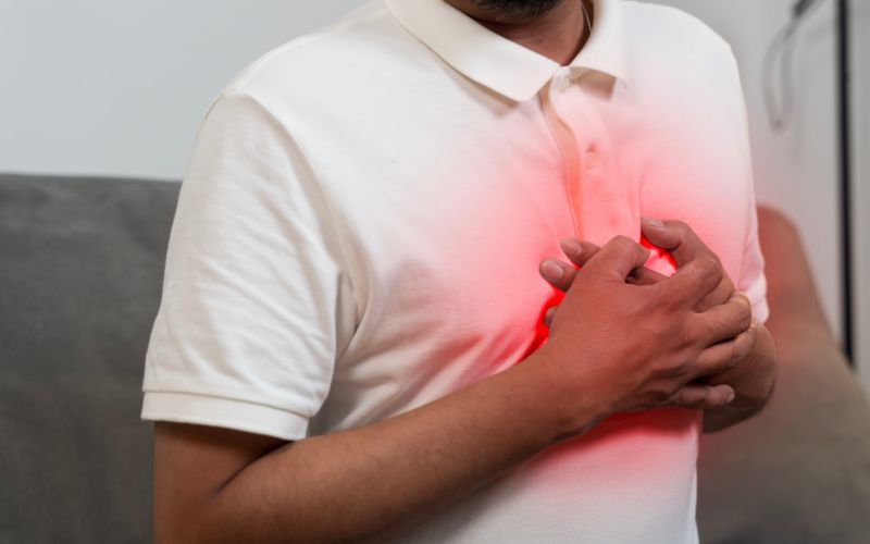 Mężczyzna trzymający się za klatkę piersiową z czerwoną poświatą symbolizującą ból.