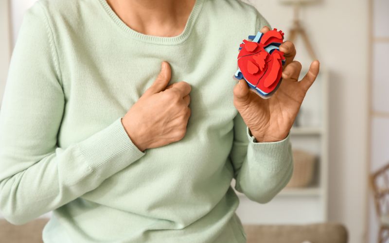 Kobieta trzymająca się za klatkę piersiową i trzymająca w dłoni model serca.