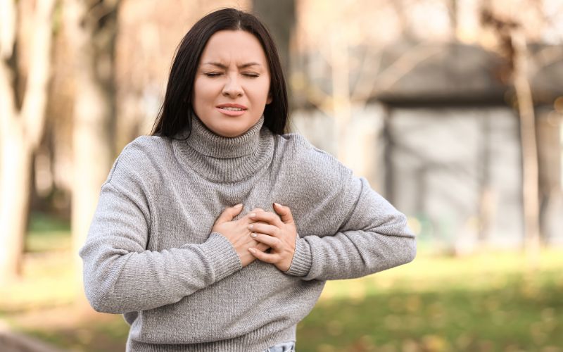 Kobieta trzymająca się za klatkę piersiową z wyrazem bólu na twarzy.